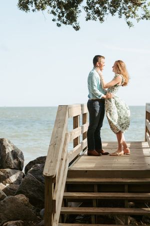 Engaged couple during engagement portraits on Saint Simons Island, near Sea Island with the wind blowing them, the ocean and boats behind