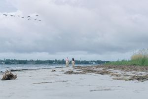 Couple riding horses with scenic view of the St. Simons Island lighthouse behind them during their engagement and proposal photography