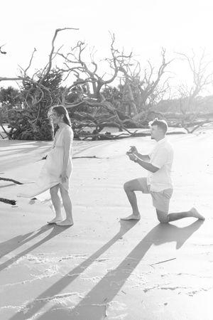 man kneeling waiting to ask woman to marry him on jekyll island georgia during a surprise proposal at Driftwood Beach