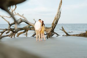 Couple embracing at Driftwood beach engagement session by water and fallen oak trees in the Golden Isles of Glynn County Georgia
