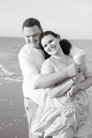 Couple embraces on Jekyll Island beach Corsair Beach in a black and white photo during engagement photo session at sunset with Lindy Rebro