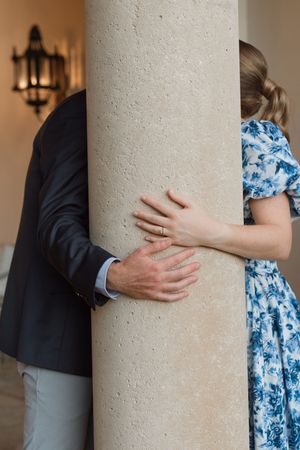 Couple newly engaged on Sea Island, GA sneaks a kiss behind the column at the resort grounds during surprise proposal photo shoot