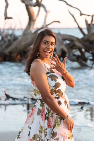 Happy bride-to-be flashes a smile and her new ring during a surprise sunrise picnic engagement during a beach proposal photography session