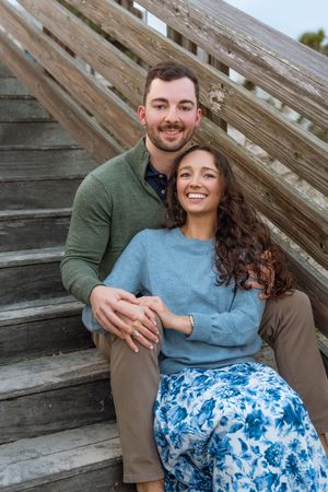 Newly engaged couple seated on stairs near beach during proposal and engagement photos on Jekyll Island, near Sea Island