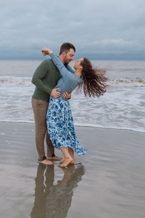Dramatic, rainy, windy october engagement portrait of young couple dancing on the beach after proposal during portrait session