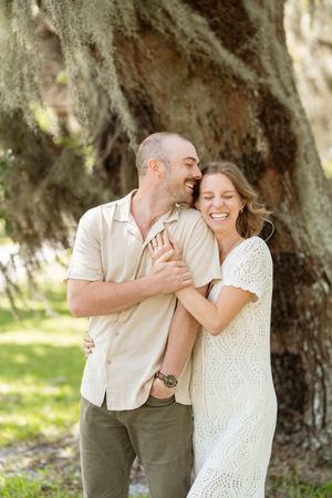 couple smiling with oak trees behind them during simple and sweet engagement with dog on jekyll island proposal
