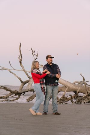 Winter proposal on Driftwood beach, couple pops the champagne cork and closes eyes during candid photo