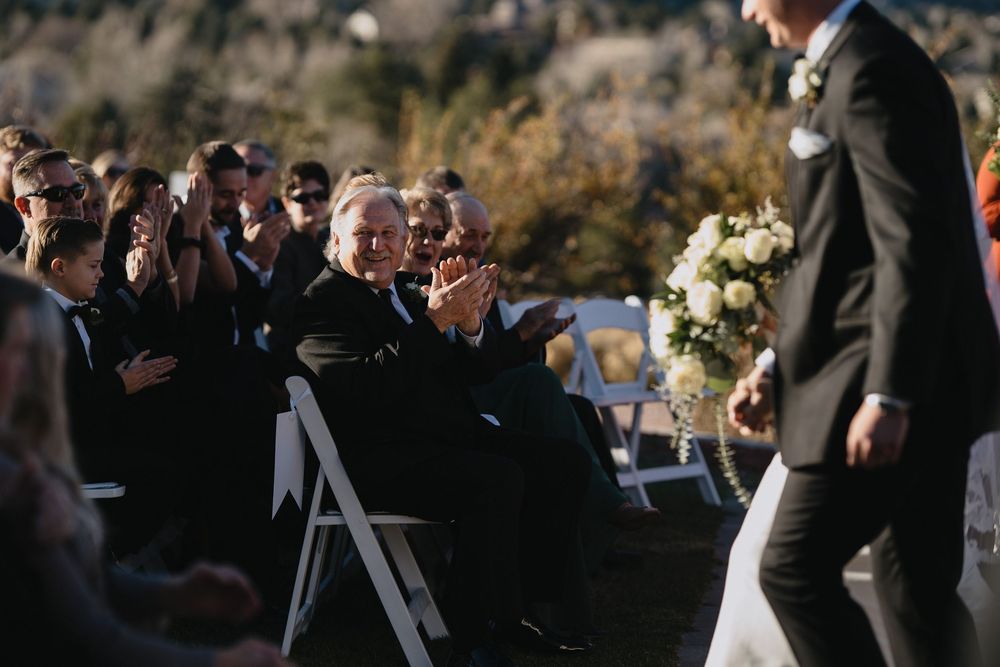 Guests clapping and celebrating as the groom walks down the aisle at an outdoor wedding ceremony.