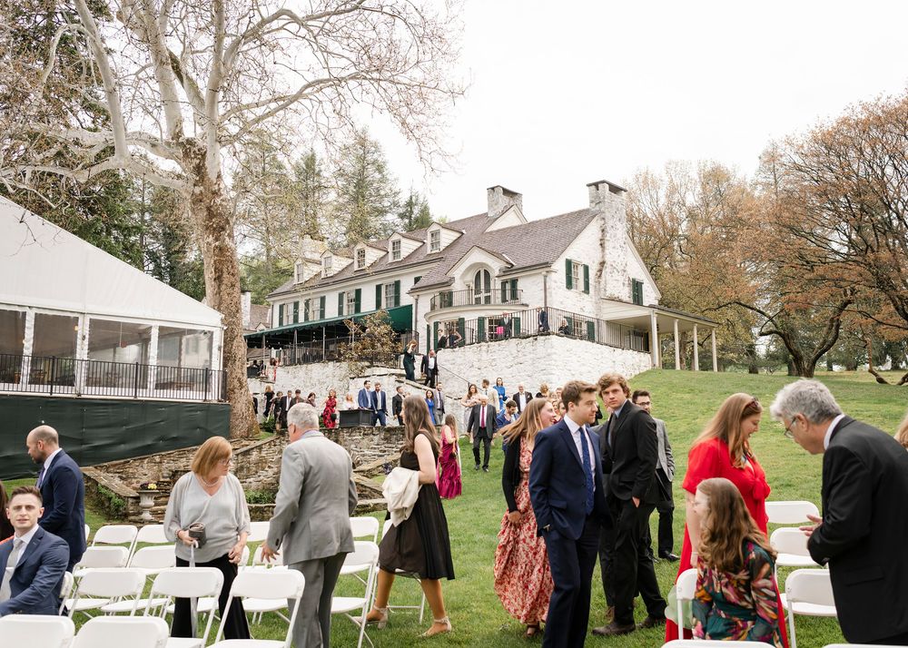 Elegant outdoor wedding reception on lush green lawn beside a grand white manor house with guests mingling.