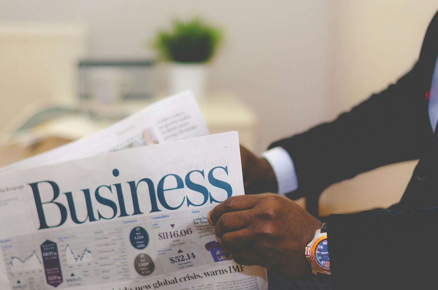 A businessman in a suit reads a Business newspaper, with charts and financial data visible on the page.