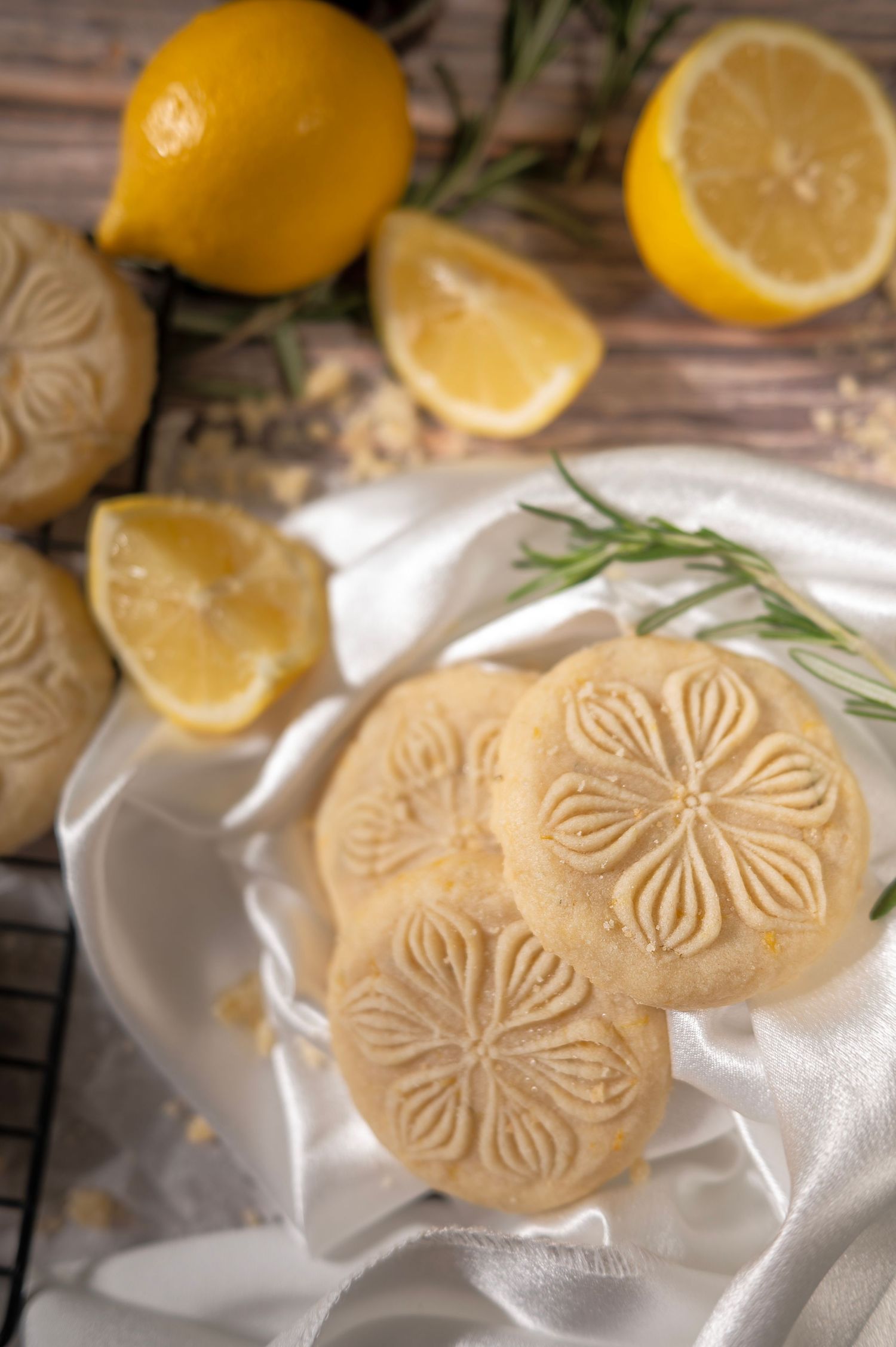 Lemon shortbread cookies with floral embossed design on white cloth with fresh lemons and rosemary.