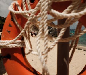 Orange life preserver ring with rope on a tropical beach, with people and large rocks visible in the background.