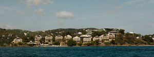 Panoramic view of luxury hillside homes overlooking turquoise Caribbean waters under partly cloudy skies.