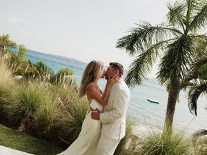 Couple shares romantic kiss surrounded by tropical palms and turquoise ocean at beach wedding.