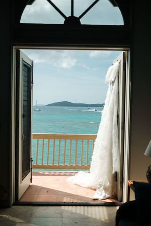 White wedding gown hanging on balcony door with stunning turquoise Caribbean ocean view beyond.