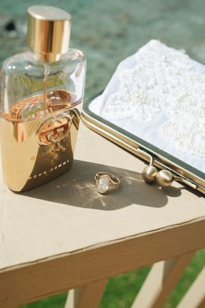 Wedding flat lay with gold perfume, diamond ring, pearl earrings, and beaded clutch.