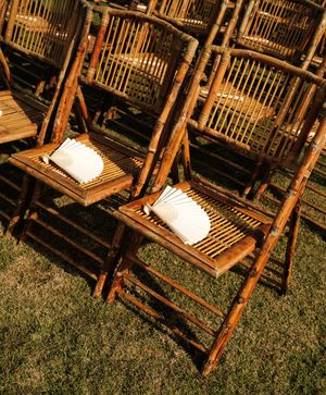 Rustic bamboo folding chairs with white paper fans on grass at an outdoor wedding ceremony.