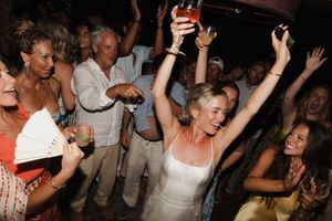 Bride in white dress dancing joyfully with guests at an outdoor wedding reception party.