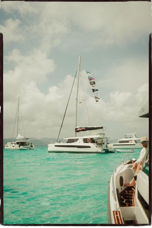 White catamaran with colorful signal flags anchored in stunning turquoise Caribbean waters on a cloudy day.