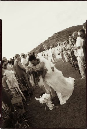Vintage sepia photo of bride and groom kissing along outdoor wedding ceremony aisle.