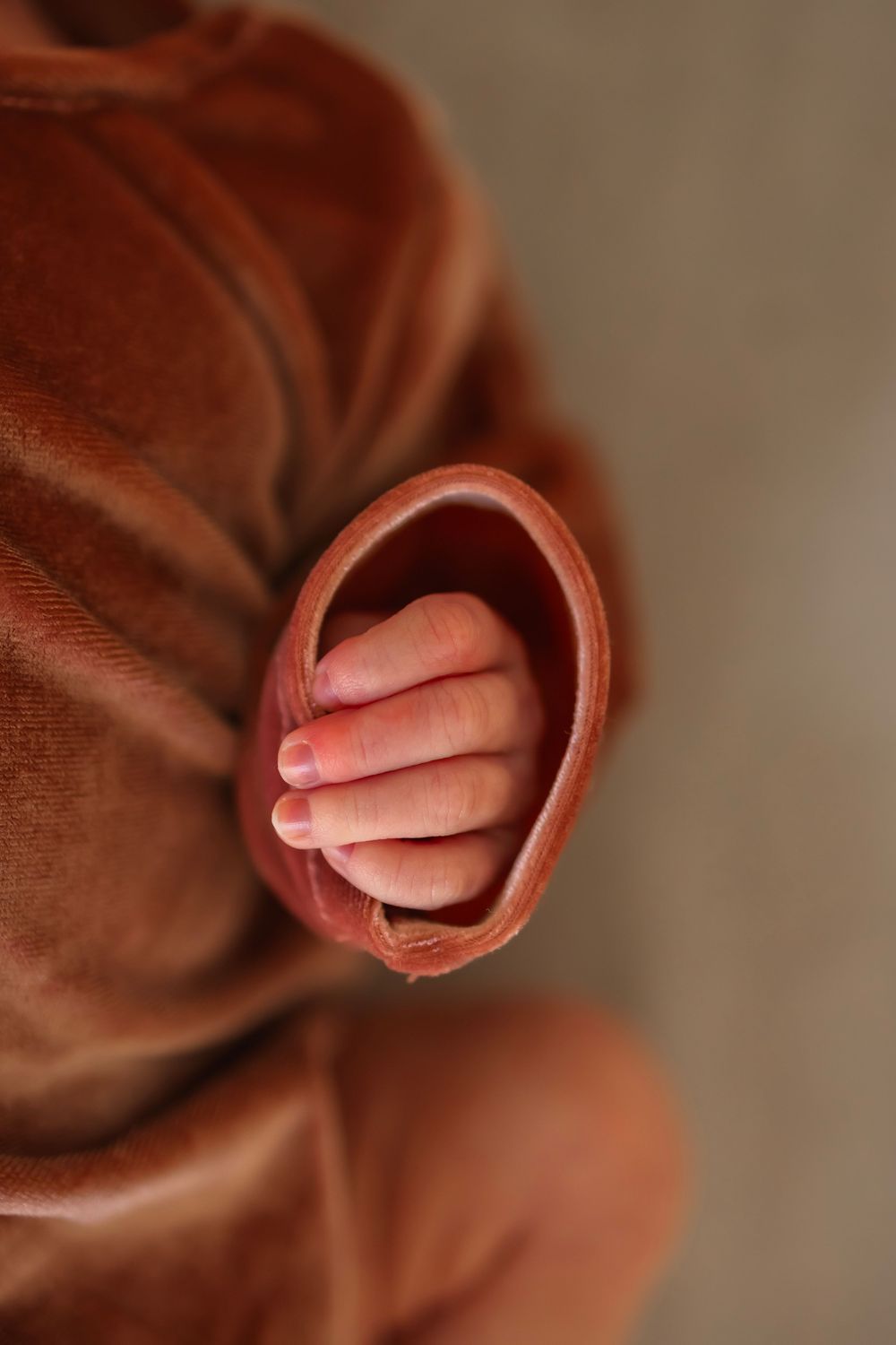 Close-up of a baby's tiny hand peeking out from a soft brown velvet outfit sleeve.