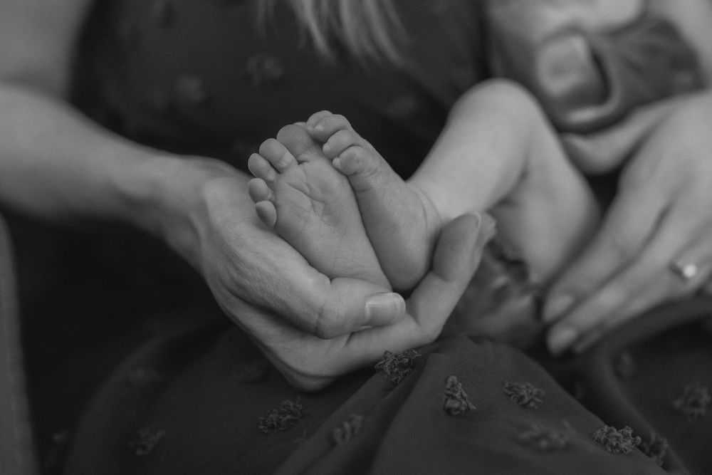 Black and white photo of adult hands gently cradling tiny newborn baby feet.