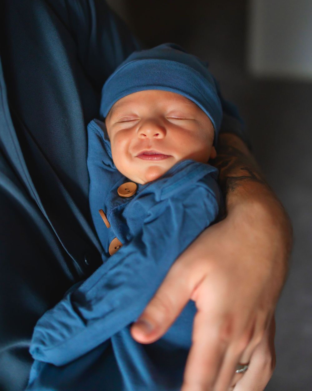 Newborn baby sleeping peacefully in blue outfit and hat, cradled in parent's arms.