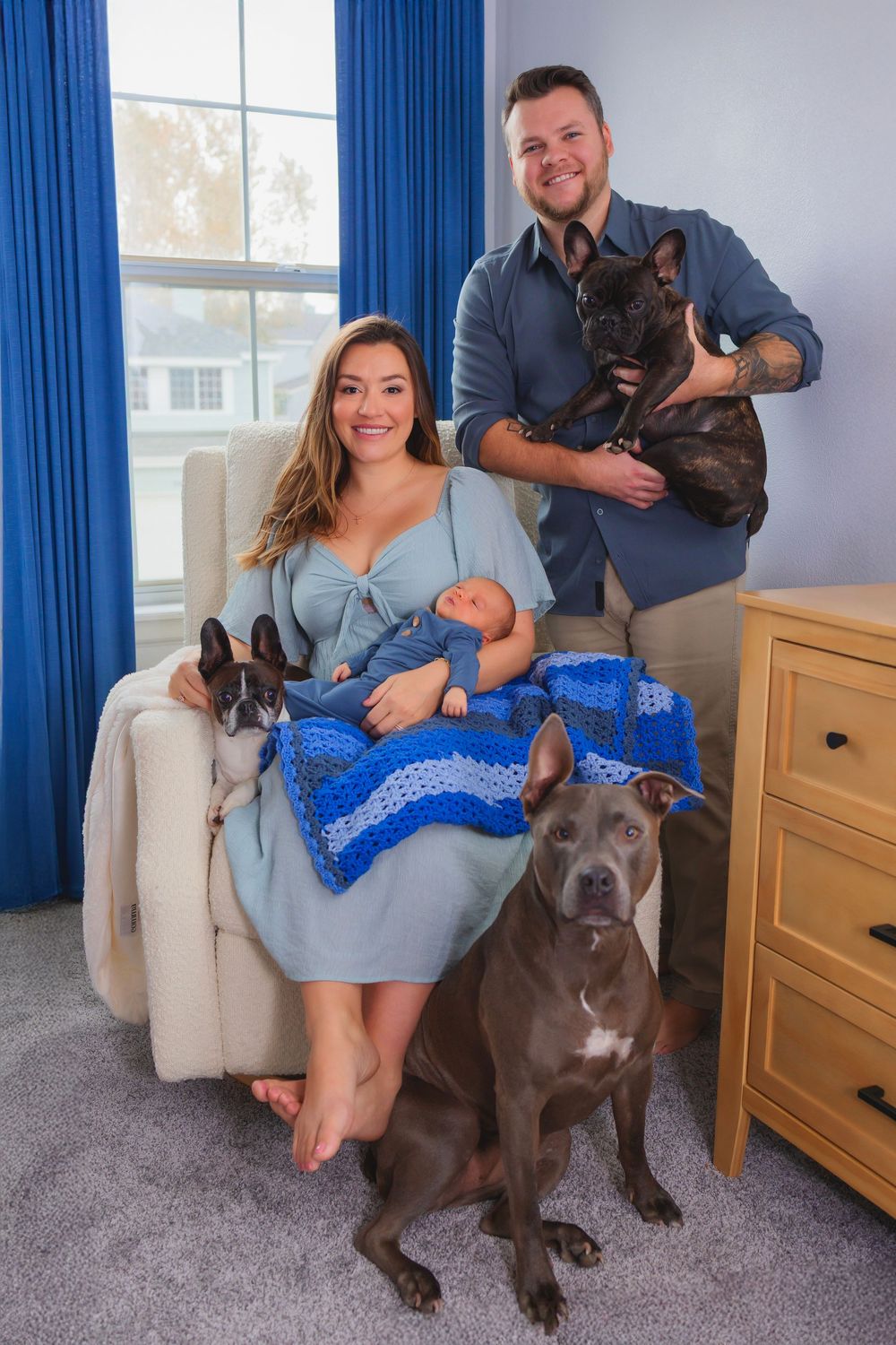 Family portrait with newborn baby, two pit bulls, and a French bulldog in a blue-themed nursery room.