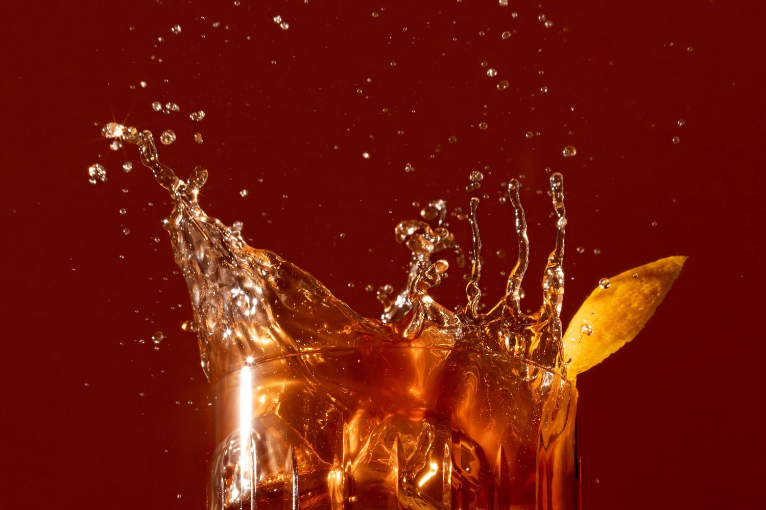 A dramatic splash of iced tea with a lemon slice against a deep red background.