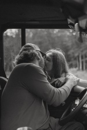 Black and white photo of a couple sharing a kiss inside a vintage truck cab.