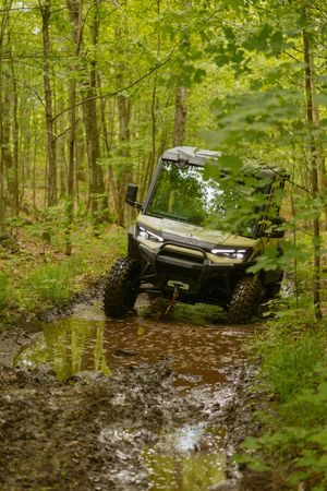 A green UTV splashes through a muddy trail in a lush forest.