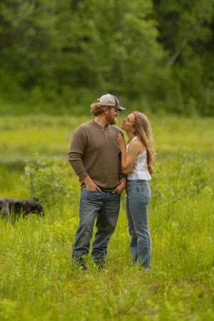 Couple gazing lovingly at each other in a lush green meadow, man in cap and woman in white top.