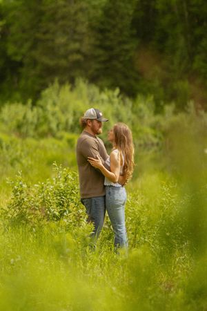 Romantic couple embracing in a vibrant green field surrounded by lush foliage and trees.