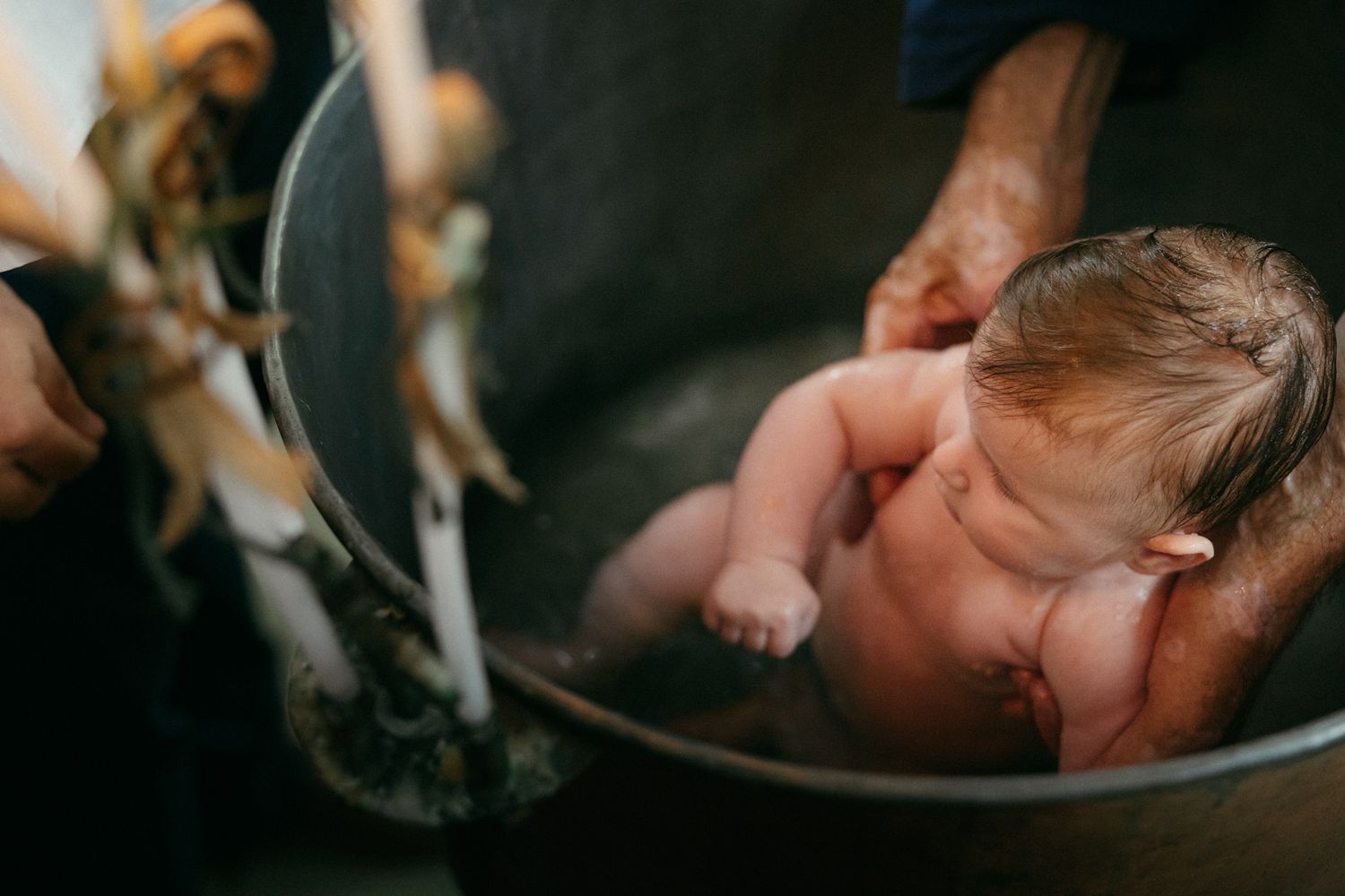 Newborn baby being bathed in a metal bowl, gently supported by adult hands during first bath.