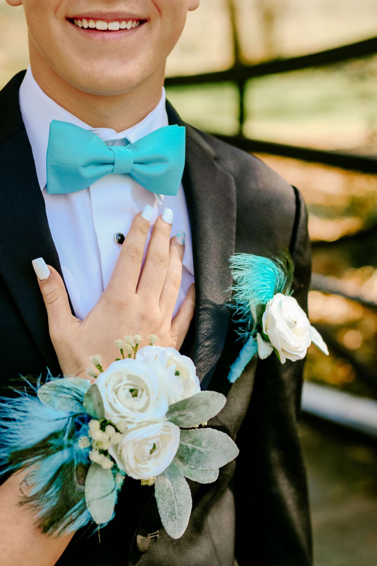 Formal attire with turquoise bow tie and white floral boutonniere with feather accents.