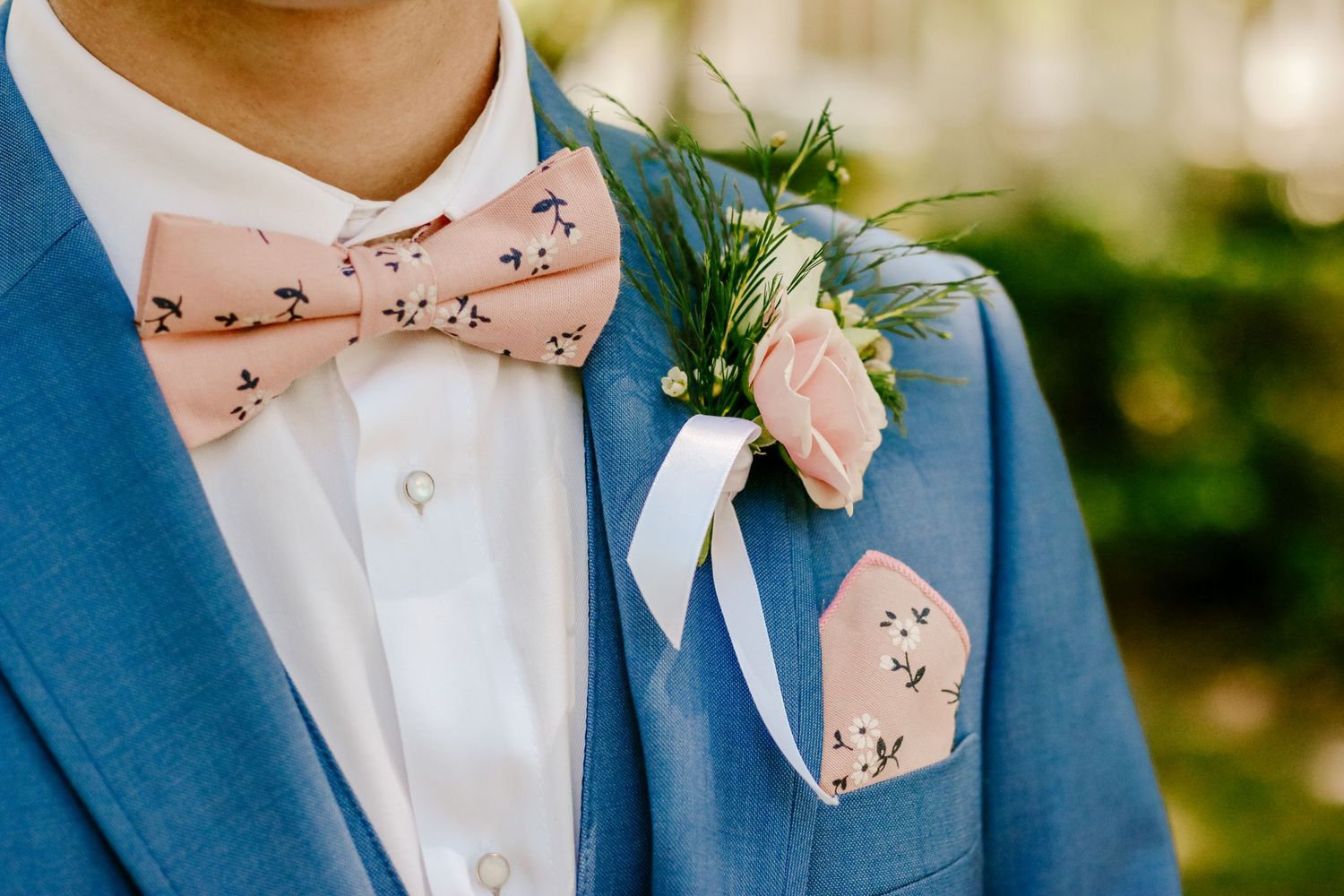 Close-up detail of a blue suit jacket with floral bowtie and white boutonniere.