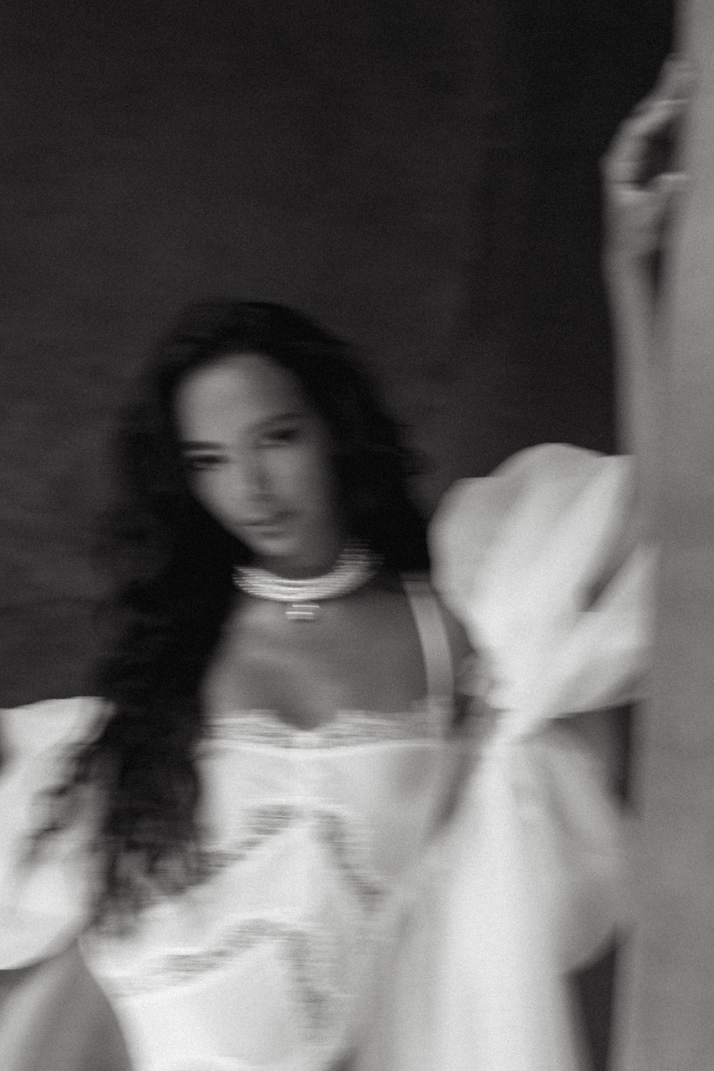 Artistic blurred black and white portrait of dark-haired bride in white lace lingerie robe.