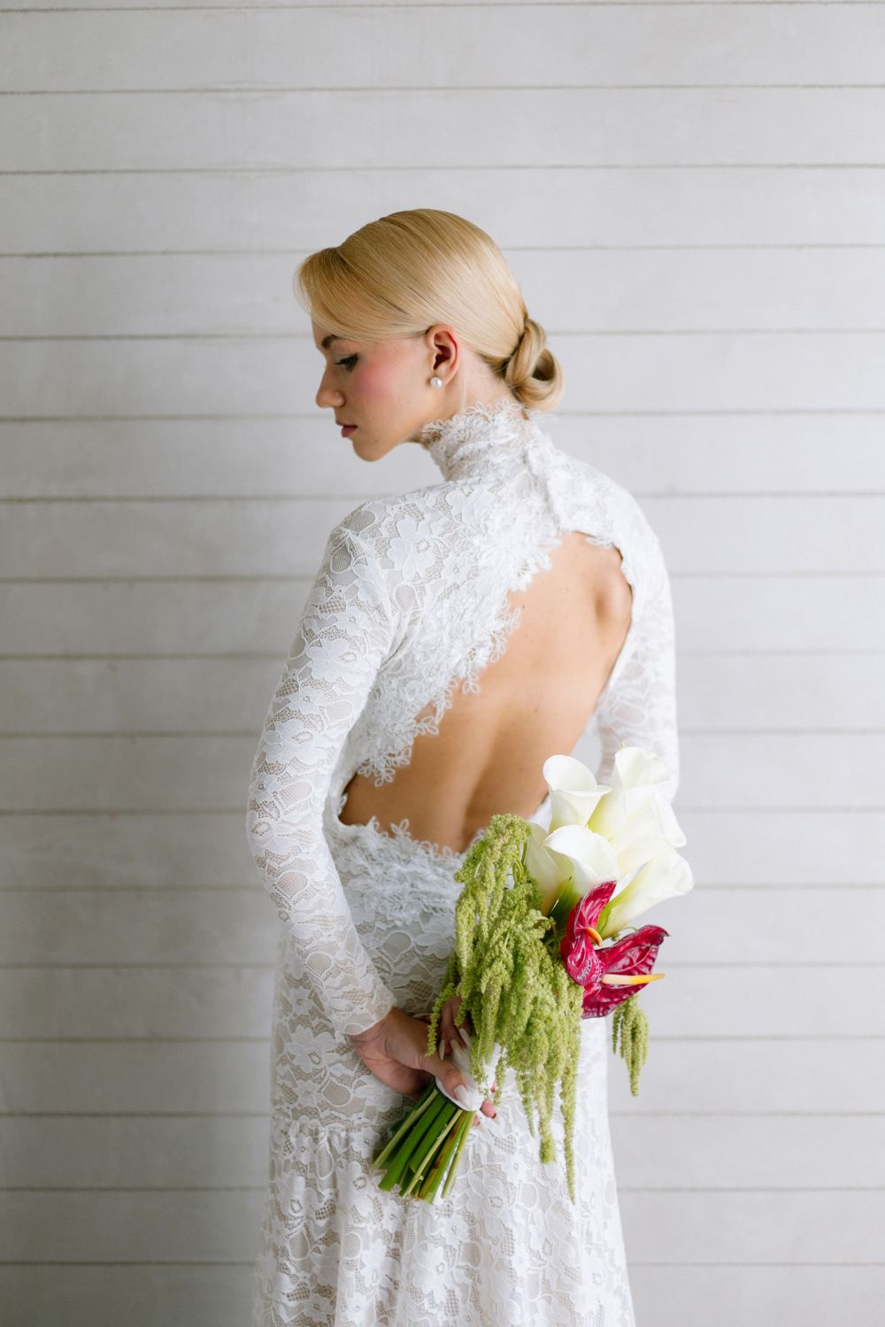 Bride in long-sleeve open-back lace wedding gown holding colorful calla lily bouquet.