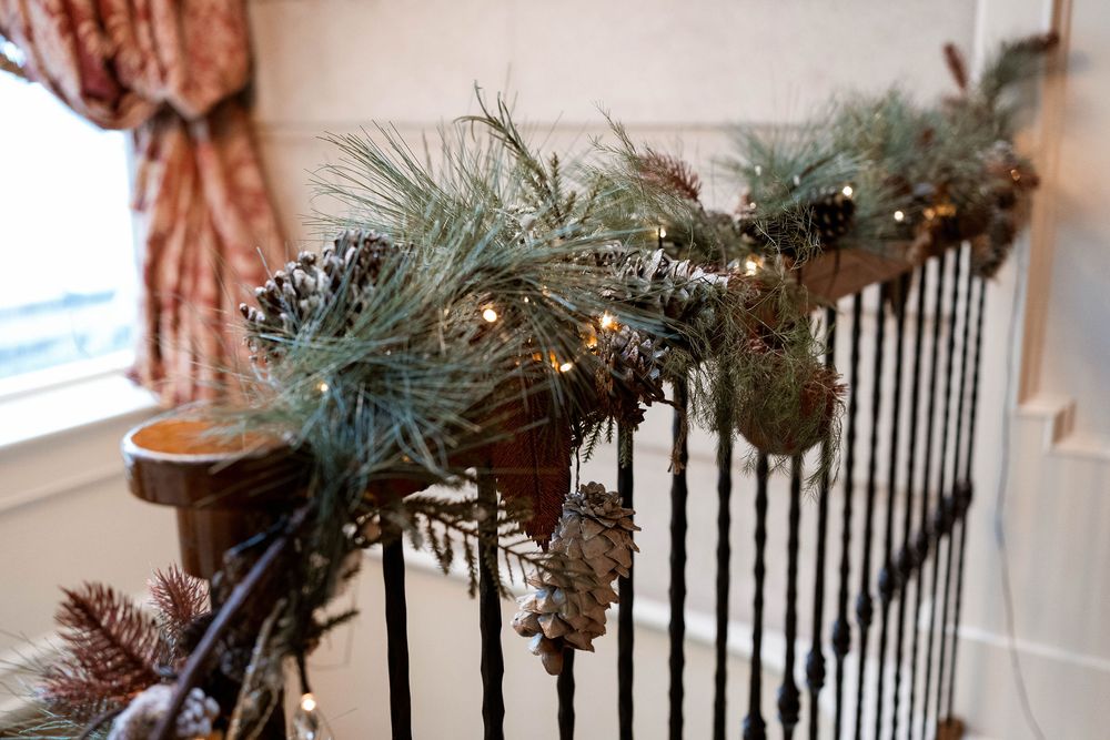 Christmas garland with pine cones and warm lights decorating a staircase railing in elegant home.