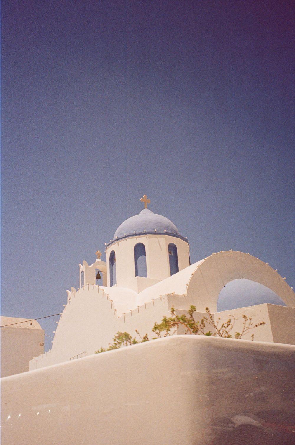 White-washed Greek Orthodox church with iconic blue dome and gold cross against clear blue sky.