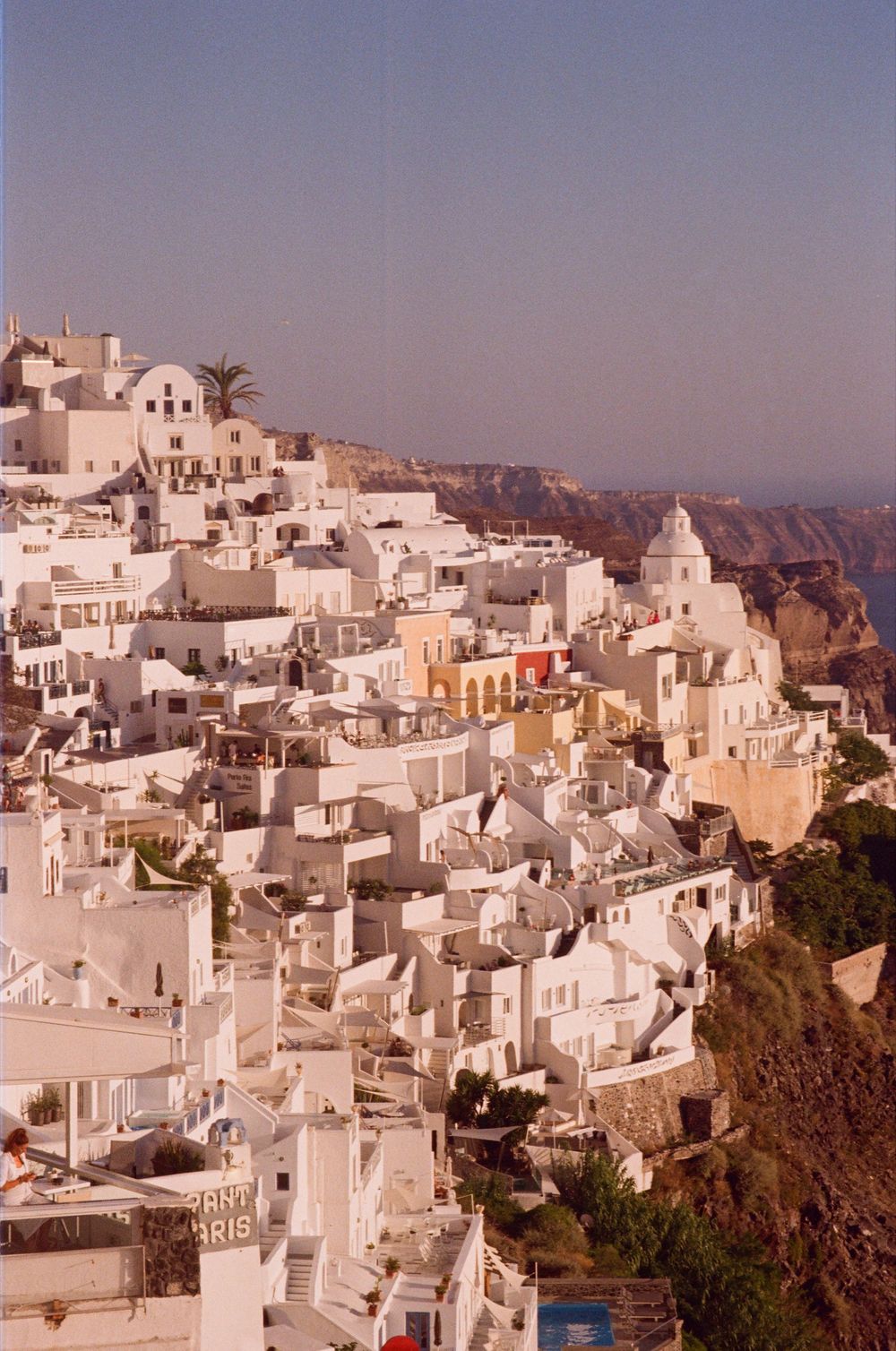 Panoramic view of white-washed buildings cascading down cliffs of Fira, Santorini, Greece.