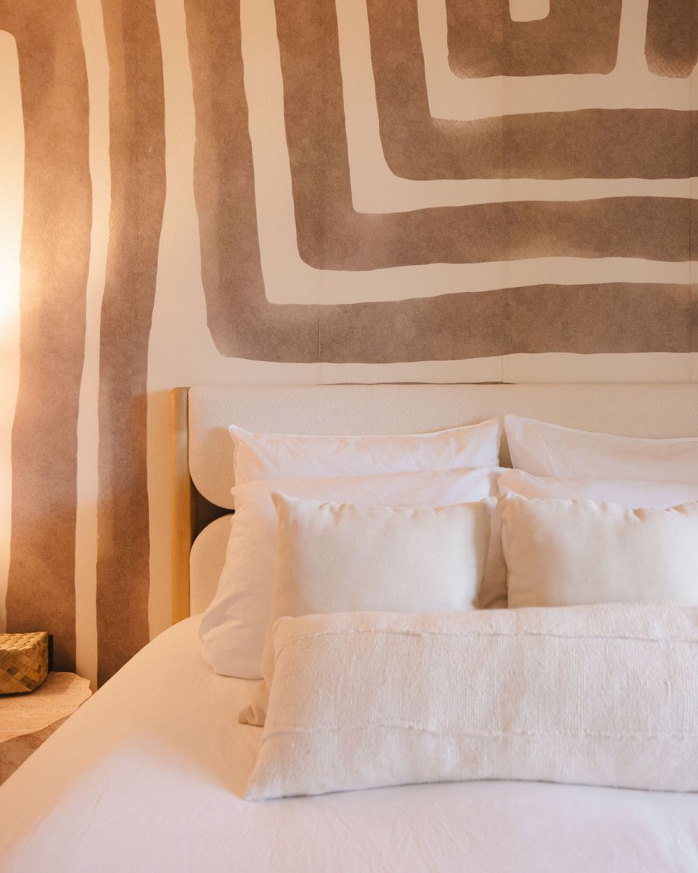 Minimalist bedroom with white pillows on a bed beneath a large beige geometric spiral wall mural.