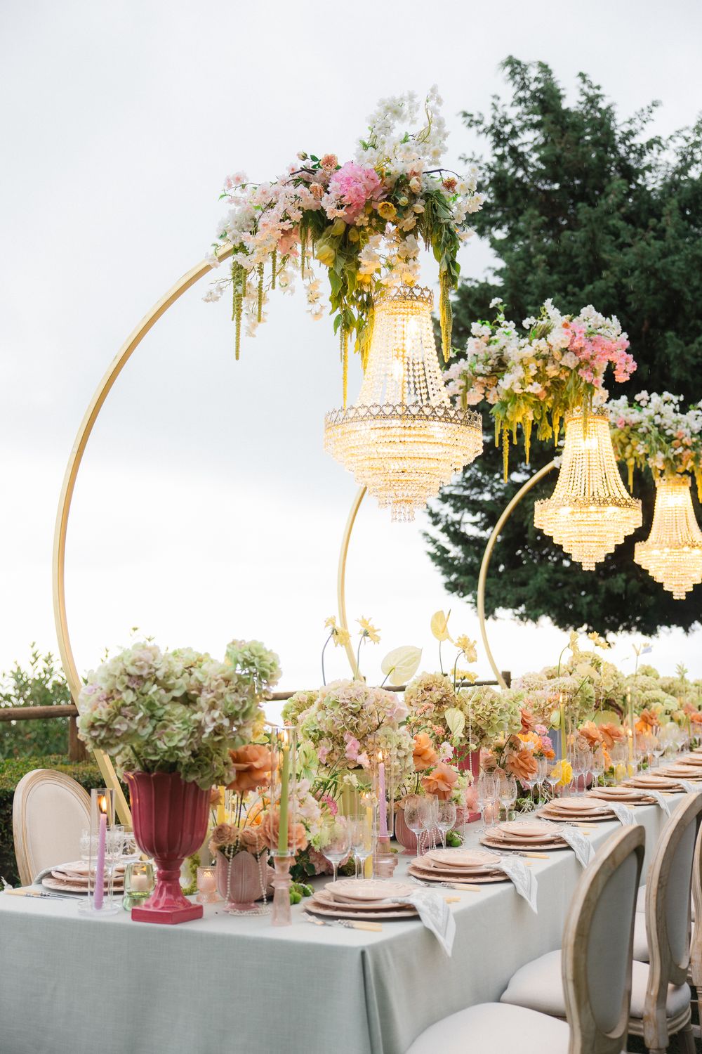 Elegant outdoor wedding reception table with crystal chandeliers, floral arrangements, and gold accents.