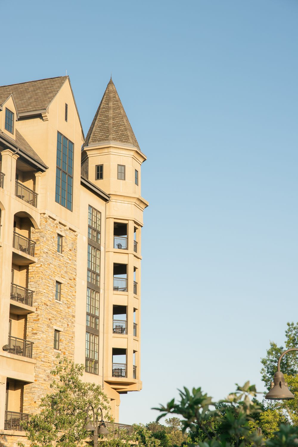 Luxury castle-style hotel tower with stone facade, arched windows, balconies, and conical turret against clear blue sky.