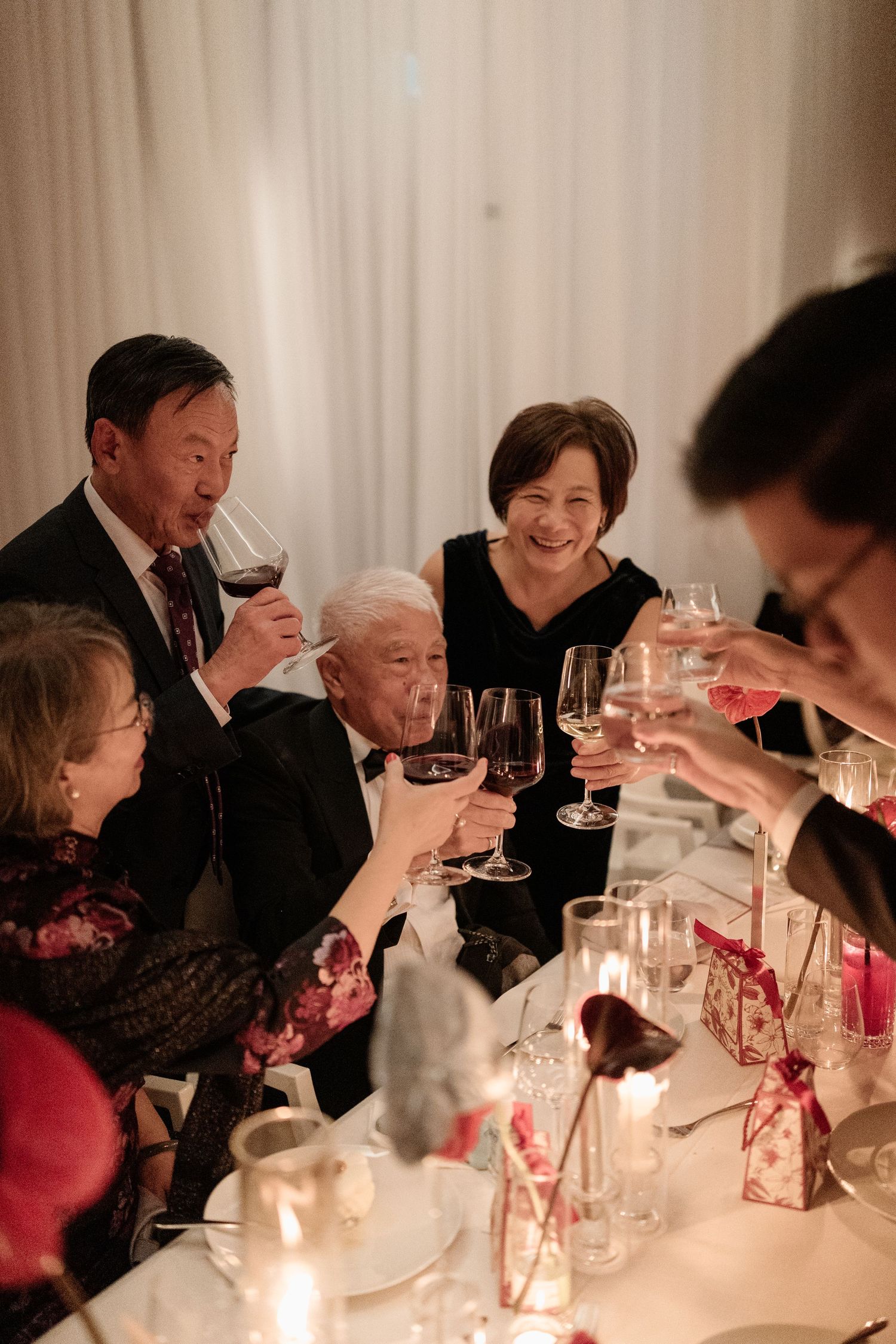 Family group raising wine glasses in a celebratory toast at a formal candlelit wedding reception.