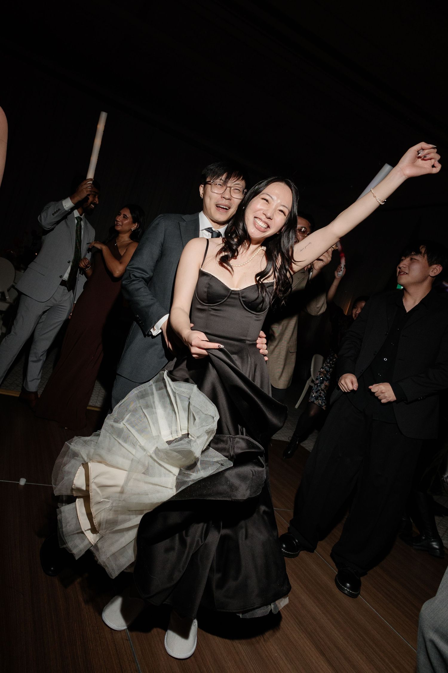 A joyful couple dancing energetically at a wedding reception, woman in black gown with tulle skirt.