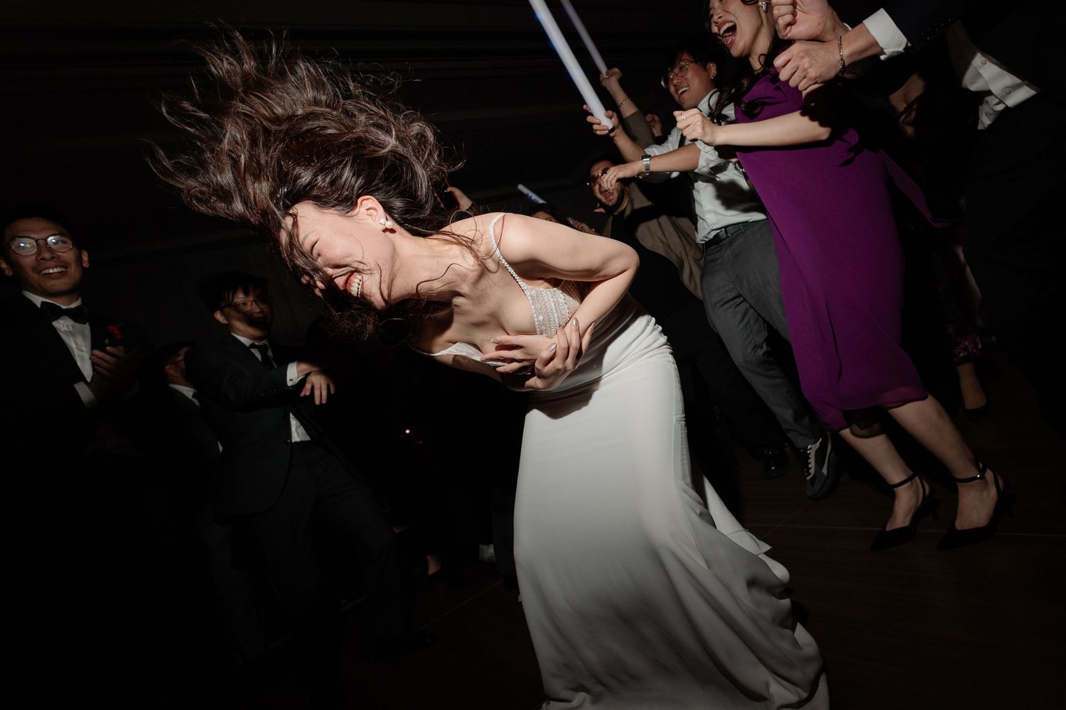 Bride in white gown dancing energetically with hair flying at a lively wedding reception celebration.