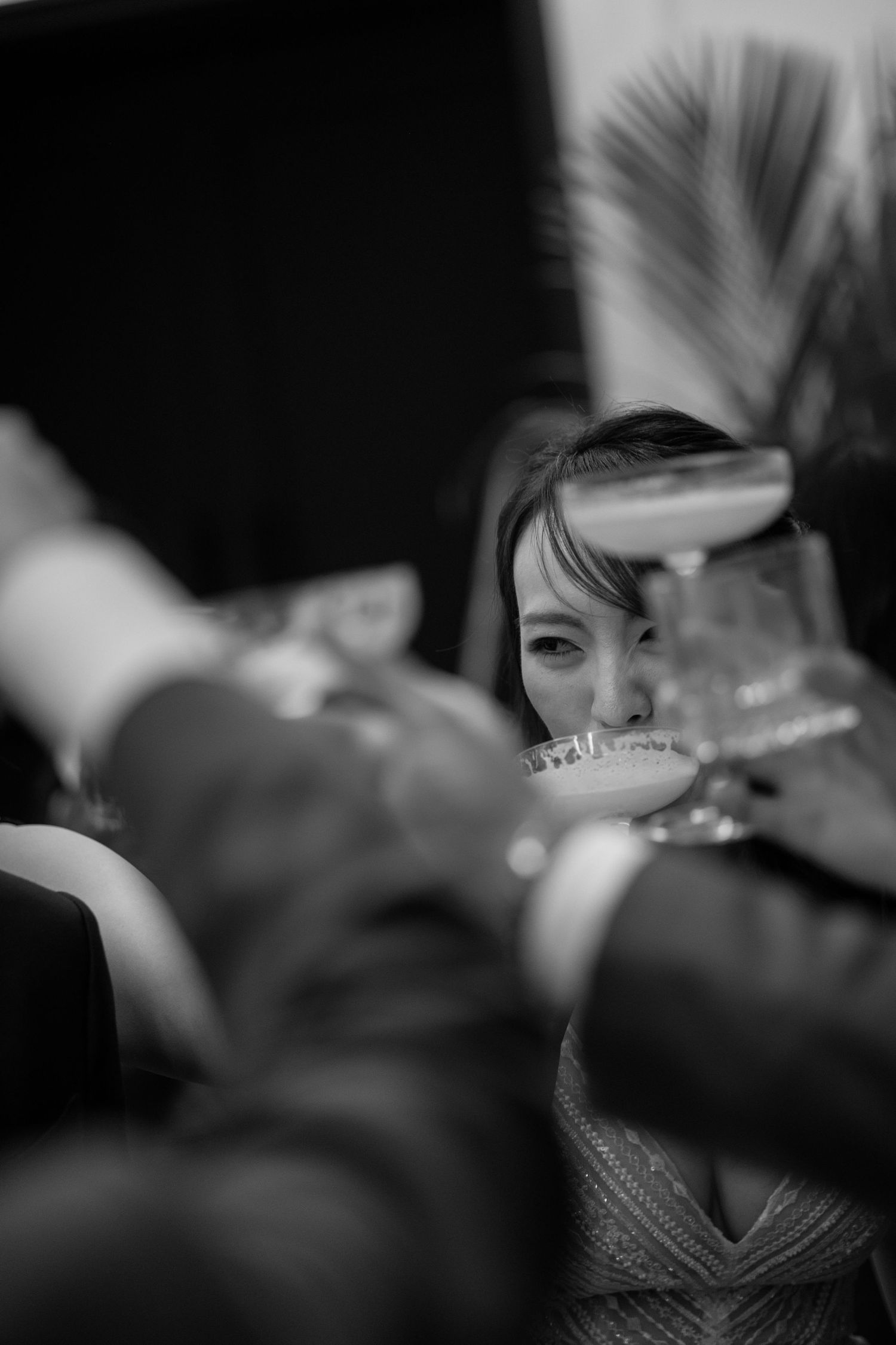 Black and white photo of a smiling woman raising a glass in a celebratory toast with friends at a party.