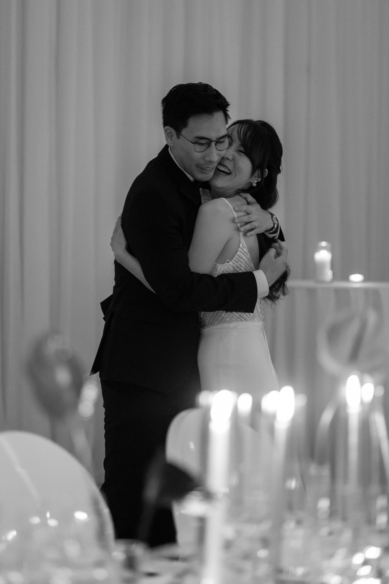 Bride and groom share a tender embrace during their first dance at a candlelit wedding reception.