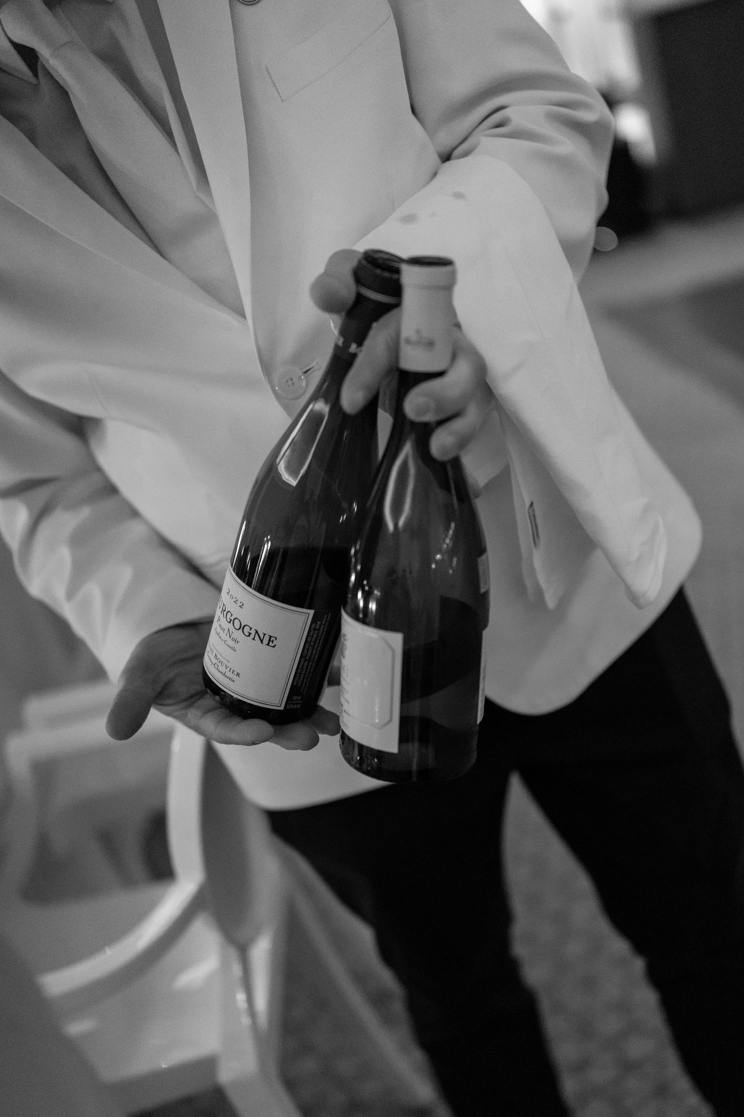 Wedding waiter in white jacket carrying two bottles of Bourgogne wine at a wedding reception.
